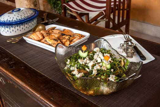 Rustic table with dishes of grilled salmon, salad and sauteed potatoes