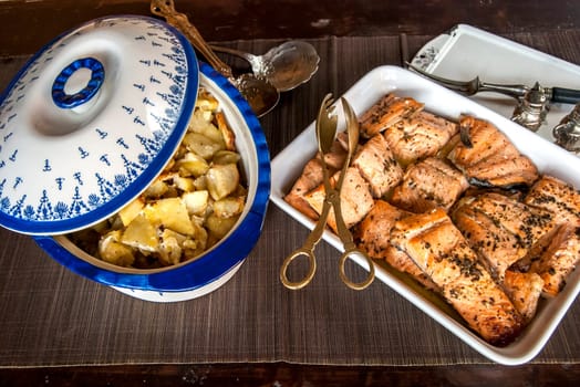 Rustic table with dishes of grilled salmon and sauteed potatoes