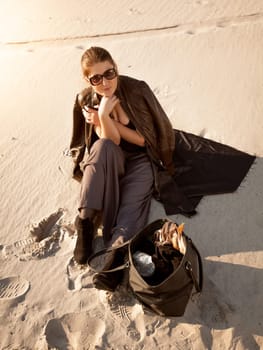Photo of lonely woman sitting on sand dune with bag