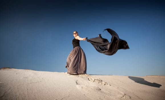 Photo of woman with black cloth walking on sand dunes