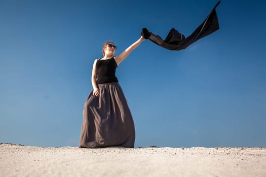 Beautiful woman in long dress with black cloth standing on sand dune