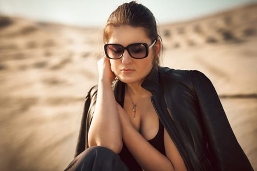 Closeup portrait of sexy woman in sunglasses sitting on sand dune
