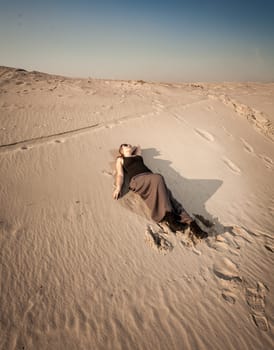 Beautiful woman in dress lying on sand dune at desert