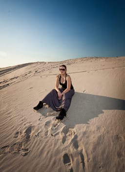 Beautiful woman in dress sitting on sand dune