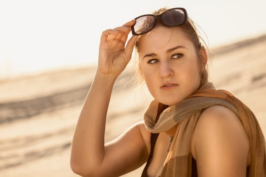Toned portrait of beautiful woman with sunglasses and scarf at desert
