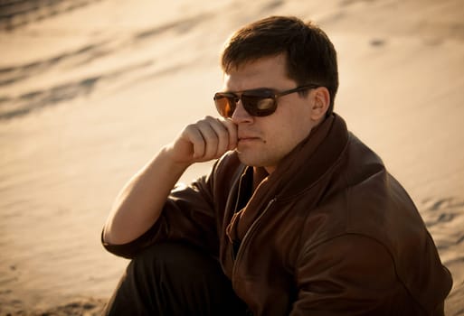 Closeup portrait of handsome man in sunglasses sitting on sand dune