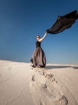 Full length portrait of woman in long dress holding long cloth on sand dune
