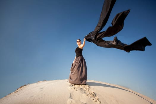 Photo of sexy woman holding black cloth on sand dune at windy day