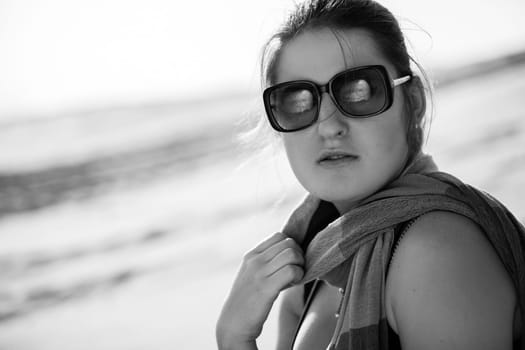 Black and white closeup portrait of woman in sunglasses and scarf against sand dunes