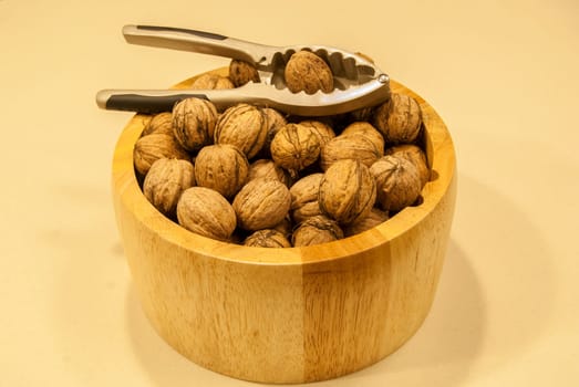 Wooden bowl with walnuts and nutcracker on a light background