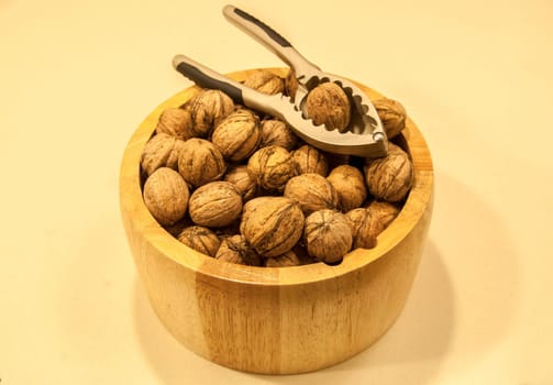 Wooden bowl with walnuts and nutcracker on a light background