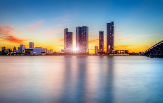 Miami city skyline panorama at dusk with urban skyscrapers over sea with reflection