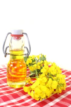 a bottle of rapeseed oil and rapeseed flowers against a white background