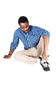 A handsome young African American man in beige pants and a blue.shirt sitting on the floor, isolated on white background..