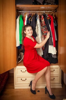 Photo of beautiful woman in red dress sitting at big wardrobe