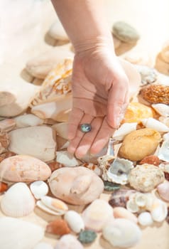 Closeup photo of female hand holding black pearl on sea shore