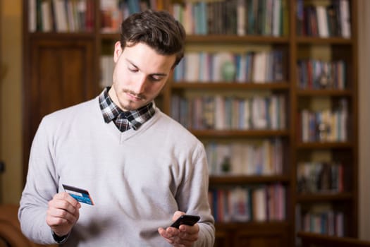 Attractive young man shopping online on mobile phone, holding credit card