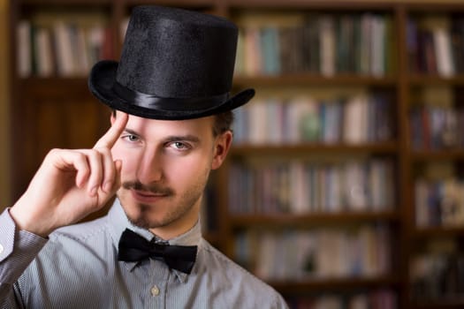 Attractive young man wearing top hat and bow tie, looking at camera. Indoors shot