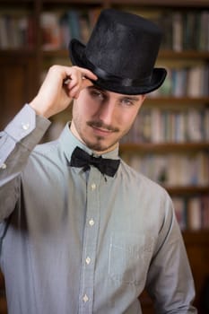 Attractive young man wearing top hat and bow tie, looking at camera. Indoors shot