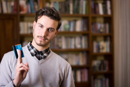 Attractive young man at home holding credit card, looking at camera