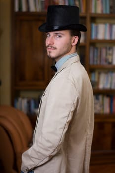 Attractive young man wearing top hat and bow tie, looking at camera. Indoors shot