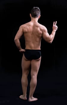 Back of muscular young man doing peace sign. Full length body shot on black