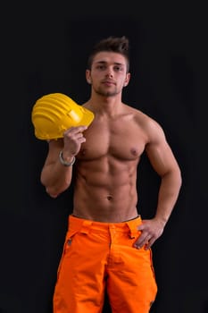 Muscular young construction worker shirtless with hardhat, isolated on black background