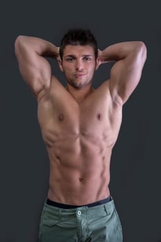 Muscular young bodybuilder showing biceps and ripped abs, smiling. Isolated on white
