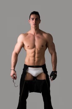 Muscular shirtless young man with handcuffs and studded glove on grey background