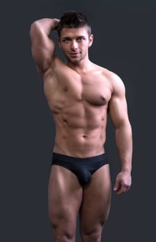 Cute muscular ripped young bodybuilder in bathing suit or underwear, smiling and looking at camera