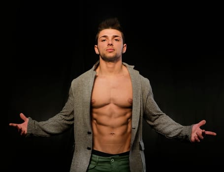Confident, attractive young man with open jacket on muscular torso, ripped abs and pecs. Arms open