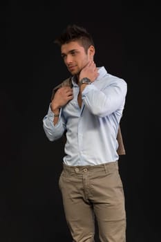 Handsome young man portrait, standing on dark background, with jacket on shoulder