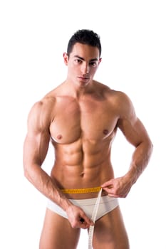 Muscular shirtless young man measuring waist with tape measure, looking at camera, isolated on white