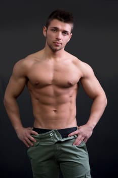 Muscular young man shirtless in relaxed pose on dark background