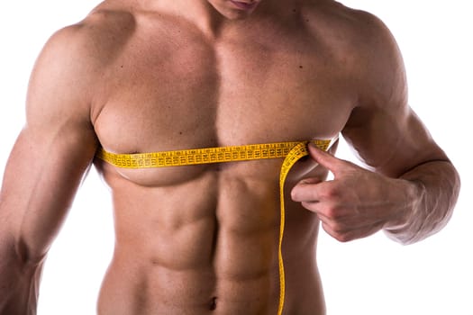 Muscular shirtless young man measuring chest and pecs with tape measure, close-up of torso on white