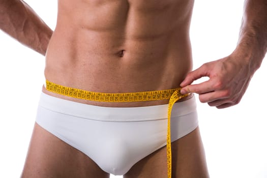 Muscular shirtless young man measuring waist with tape measure, close-up of hips and abdomen area