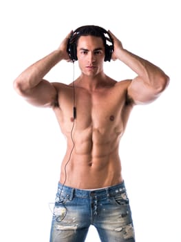 Muscular man shirtless, standing, listening to music on headphones, looking at camera
