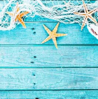 Pretty turquoise blue nautical background decorated with draped fishing net and starfish on painted rustic wooden boards with copyspace suitable as a card or party invitation, square format