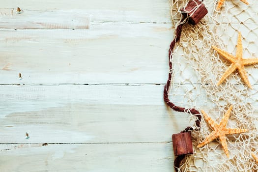 Nautical border formed of fishing net edged with corks entangled with scattered starfish on light beige wooden boards with copyspace for your text or advertisement