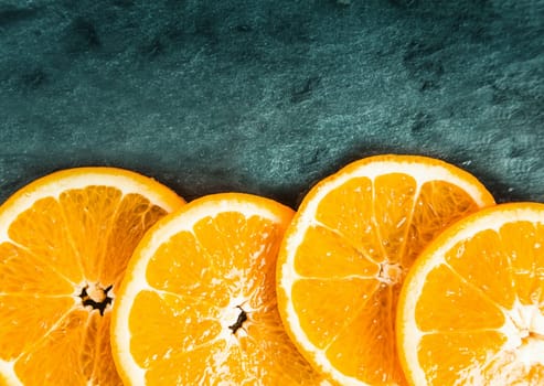 Colorful juicy fresh orange slices arranged as a lower border on textured slate with top corner vignetting and copyspace