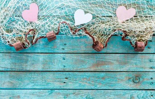 Pretty pink and white hearts in a fishing net border with corks symbolising love and romance on turquoise blue wooden boards for your Valentines,anniversary or wedding greeting, horizontal format