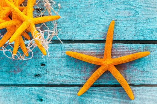 Collection of orange starfish on turquoise blue wooden boards with fishing net for a colourful nautical or marine background with copyspace