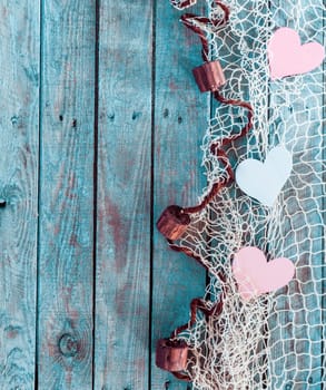 Border of romantic pink and white hearts in fishing net with an edge decoration of corks in vertical format on rustic turquoise blue boards with copyspace for your Valentine or anniversary greeting