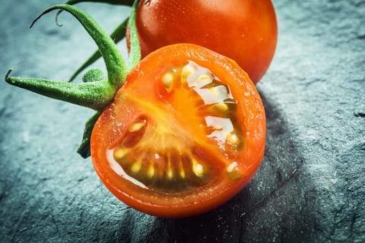 Close up of a halved juicy fresh grape tomato showing the pips and pulp with a green stalk for a healthy salad or cooking ingredient