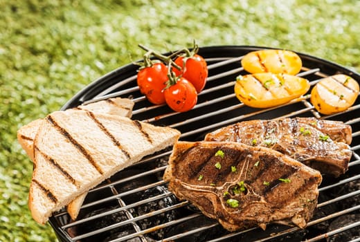 Delicious grilled lunch on a barbecue with lamb chops, tomatoes, potato and slices of toast waiting to be served on a summer day