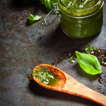 Making delicious fresh pesto sauce with fresh ground basil leaves, parmesan cheese and pine nuts mixed with olive oil and displayed in a wooden spoon on a slate counter