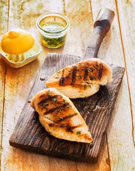 Healthy grilled chicken breasts marinated with lemon and olive oil and cooked on a summer BBQ served on an old wooden board