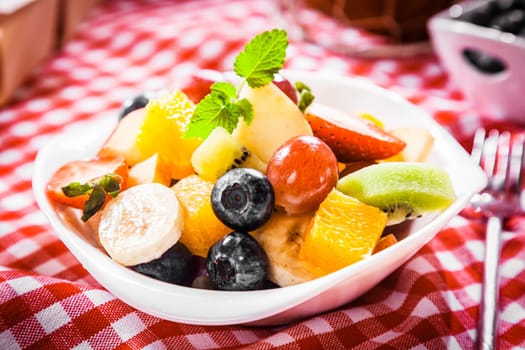 Colorful bowl of tropical fruit salad with blueberries, kiwifruit, orange, apple, banana, grapes and orange for a healthy summer picnic