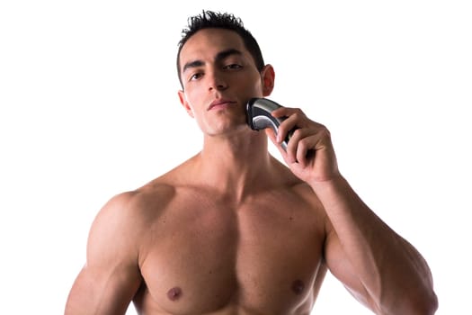 Muscular man shirtless using electric shaver, looking at camera, isolated on white