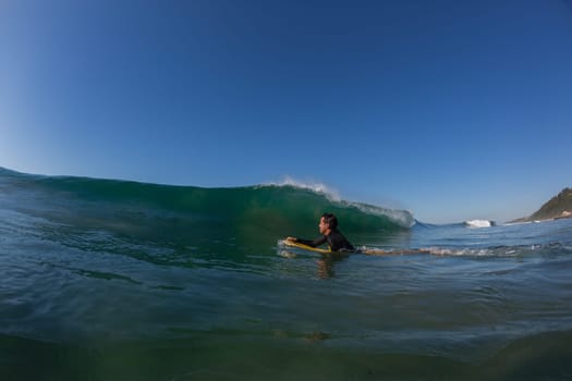 Ocean wave crashing on shallow reef with body-boarder paddling out to catch next surfing wave.